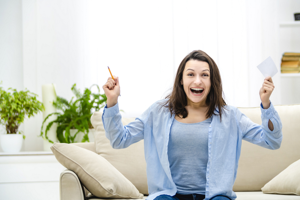 Woman excited sitting on couch after learning about free lottery tickets.